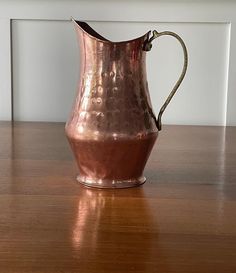 a copper colored pitcher sitting on top of a wooden table next to a white wall