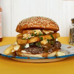 a hamburger with onions, cheese and other toppings on a bun sitting on a plate