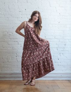 a woman standing in front of a white brick wall wearing a brown and pink dress