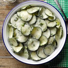 a bowl filled with sliced cucumbers on top of a wooden table next to a fork