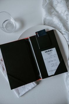 an open book sitting on top of a white plate next to a glass of water