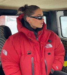 a woman sitting in the back seat of a car wearing a red jacket and sunglasses