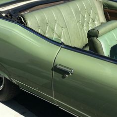 the interior of a green convertible car with its door open and seats folded back to side