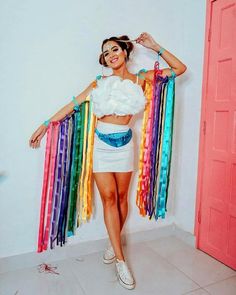 a woman in a white top and skirt with rainbow streamers around her waist posing for the camera