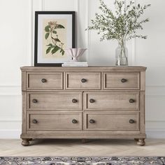 an old dresser with flowers in a vase on top and a framed photograph above it