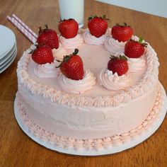 a white cake topped with strawberries on top of a wooden table