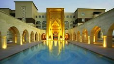 an indoor swimming pool surrounded by arches and pillars with lights on the sides at night