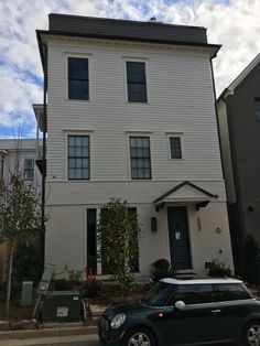 a car is parked in front of a white two story house with black shutters