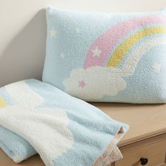 two pillows sitting on top of a wooden dresser next to a pillow with a rainbow design