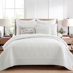 a bed with white comforter and pillows in a room next to two lamps on nightstands