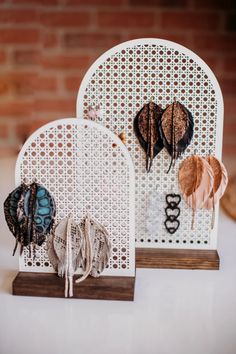 two decorative pieces are on display in front of a brick wall, one is made out of white wicker and the other has feathers attached to it