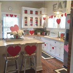 a kitchen with white cabinets and red heart decorations on the wall above the bar stools