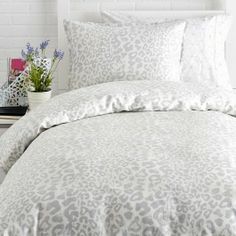 a bed with white and grey leopard print comforter set on top of it next to a plant