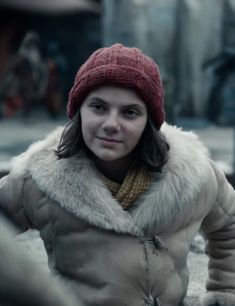 a woman wearing a red hat and coat standing in front of an old building with snow on the ground