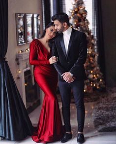 a man and woman standing next to each other in front of a christmas tree