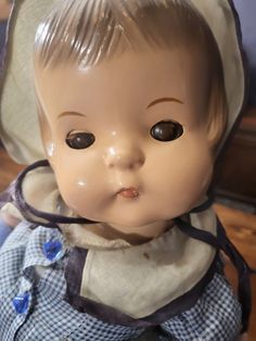 an old doll is wearing a bonnet and blue checkered dress with white trim on it's head