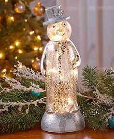 a snowman with a top hat and lights in front of a christmas tree on a table