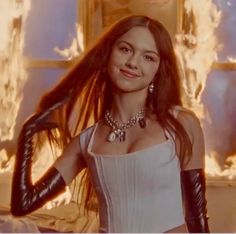 a woman with long hair and leather gloves posing in front of a fire filled wall