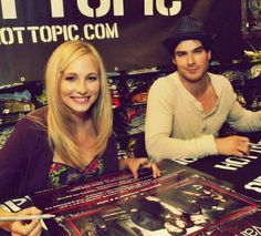 two people sitting at a table signing autographs