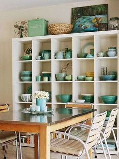 a dining room table and chairs in front of a bookcase filled with plates and bowls