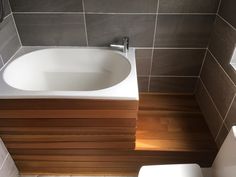 a white toilet sitting next to a bath tub in a bathroom on top of a wooden floor