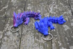 two blue and purple dragon keychains sitting on top of a wooden table