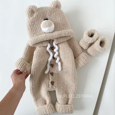 a teddy bear wearing a knitted coat and mittens is being held by someone's hand