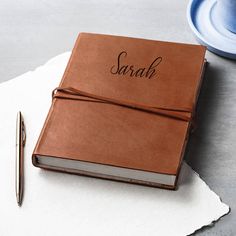 a personalized brown leather notebook with the word sarah on it and a pen next to it