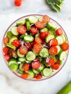 a bowl filled with cucumbers and tomatoes on top of a white countertop