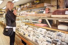 a woman standing in front of a display case filled with cheese