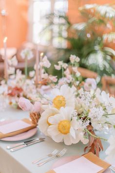 the table is set with white and yellow flowers, silverware, and napkins