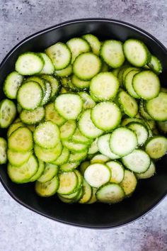 a bowl filled with sliced cucumbers sitting on top of a cement countertop