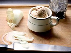 a cup filled with ice cream sitting on top of a cutting board next to a knife