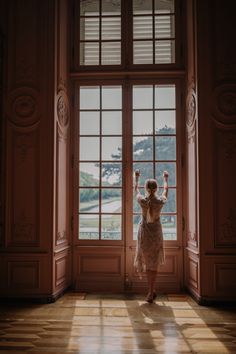 a woman standing in front of an open window with her arms up and hands raised