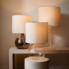 three lamps sitting on top of a wooden table next to a vase and lamp shade