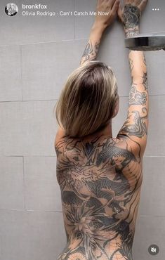 a woman with tattoos on her back standing in front of a wall