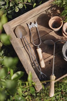 an old wooden tray with utensils and pots on it in the middle of some grass