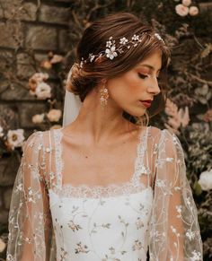 a woman wearing a wedding dress and veil with flowers in her hair is standing near a brick wall