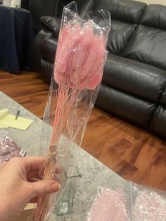 a person is holding some pink flowers in a plastic bag on a table next to a couch