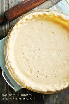 a pie crust in a glass pie dish on a wooden table with a rolling pin