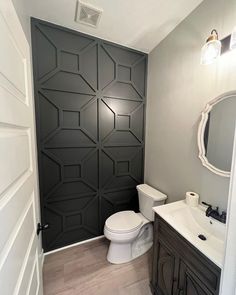 a white toilet sitting under a bathroom mirror next to a wooden sink vanity and black paneled door