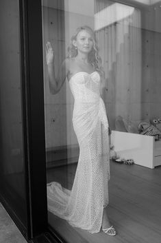 a woman in a dress is standing by a glass door and waving at the camera