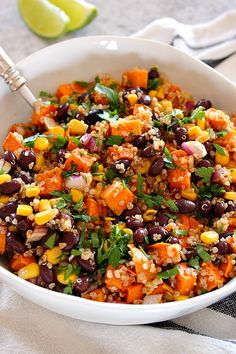 a bowl filled with black beans, corn and cilantro next to a lime wedge