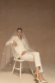 a woman sitting in a chair wearing a white suit and veil