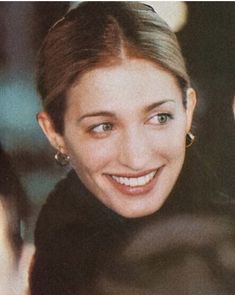 a woman smiling and looking at the camera with other people in the background behind her