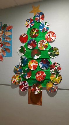 a christmas tree made out of paper plates on the wall next to a bulletin board