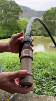 a person is holding a water hose in their hand and there is a lake behind them