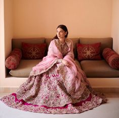 a woman sitting on top of a couch in a pink and gold dress next to pillows