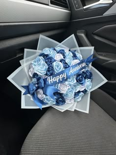 a bouquet of blue and white roses sitting in the front seat of a car with happy anniversary written on it