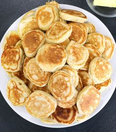 a white plate topped with pancakes next to a bowl of butter and syrup on a table